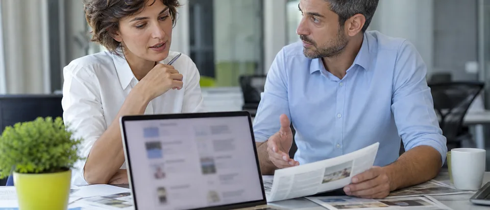 PR team reviewing press coverage on a laptop next to printed newspapers