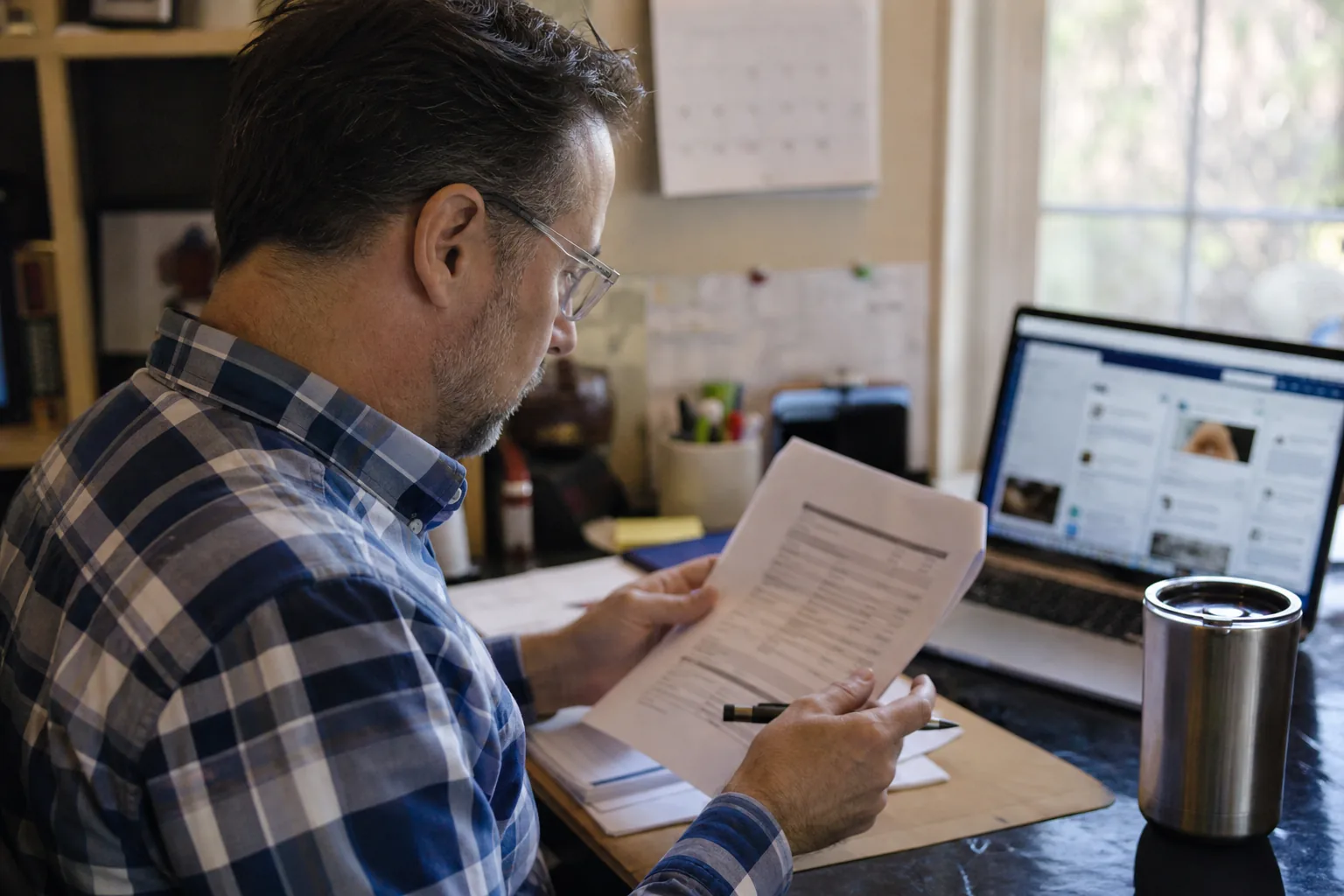 Communications manager reviewing a software renewal quote on paper next to a laptop in a small office