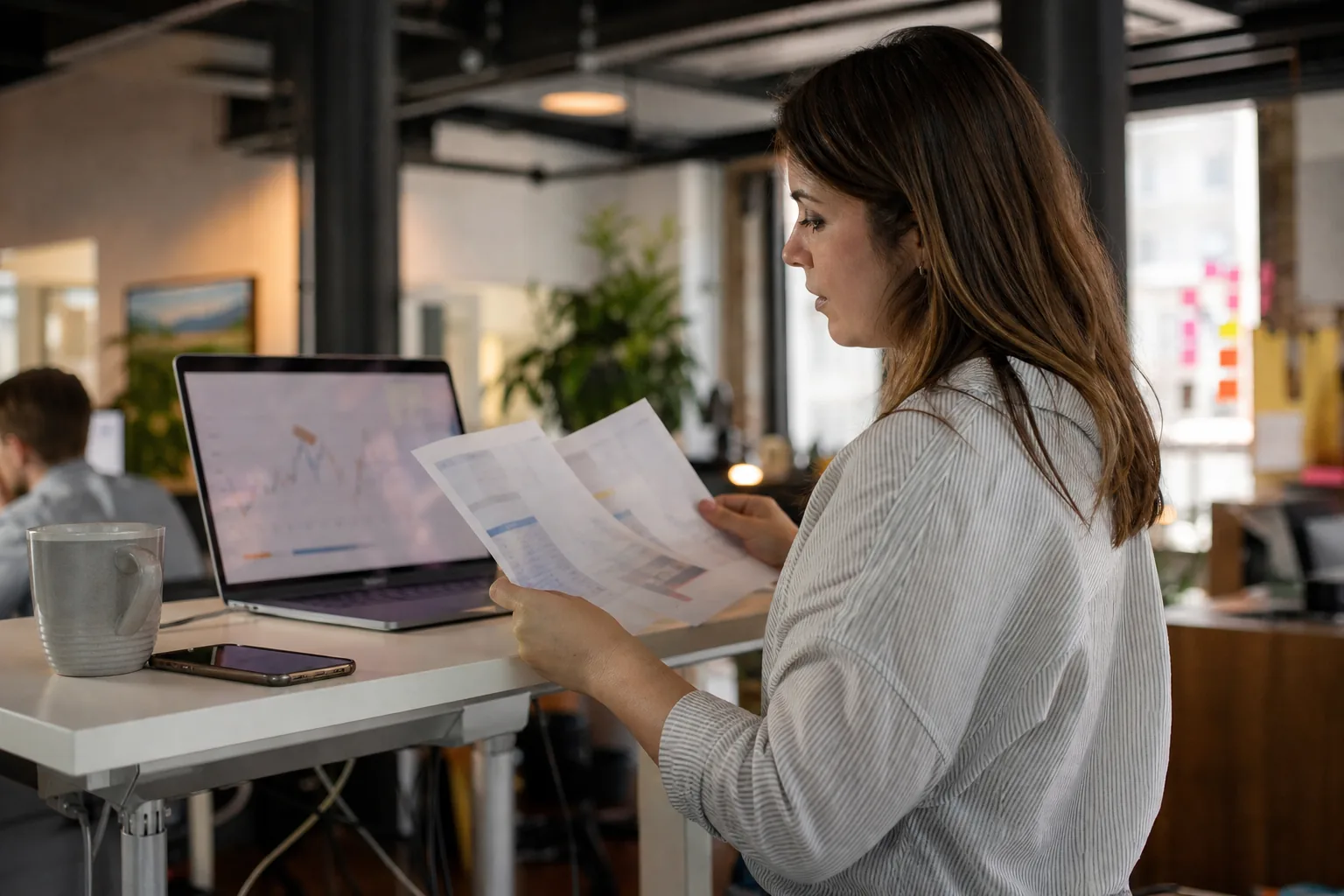 Marketing operations manager comparing two software invoices beside a laptop with a trend chart